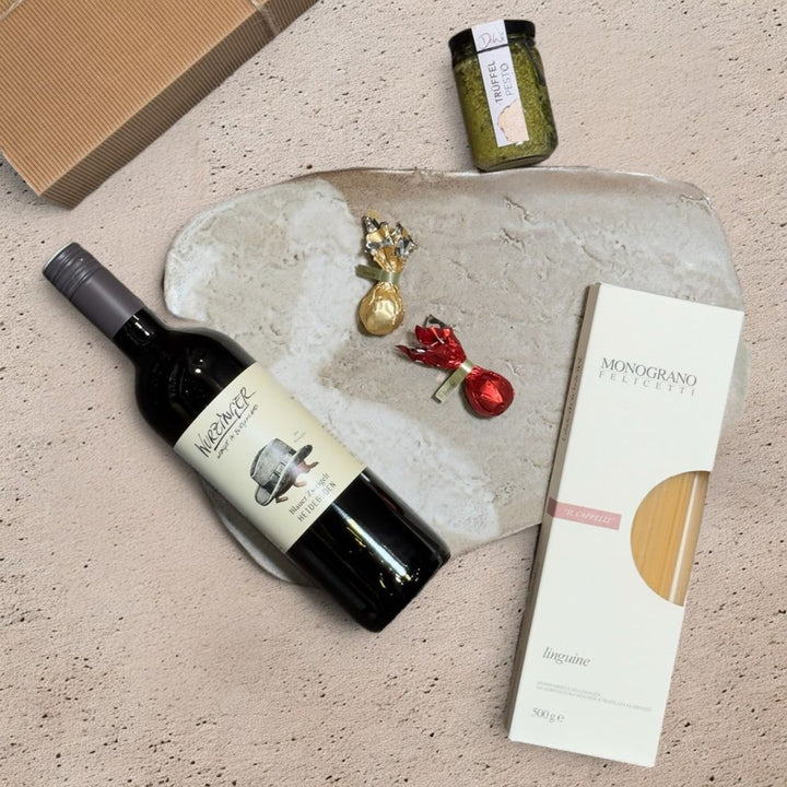 Ausgepackte Wein Geschenkbox Weihnachten mit Wurzinger Blauer Zweigelt Heideboden 2024 DeWi Pesto Trüffel Felicetti Monograno Il Cappelli Linguine 152 Venchi rote goldene Weihnachtskometen und Metall Weihnachtsmotive mit Schelle weiß gold