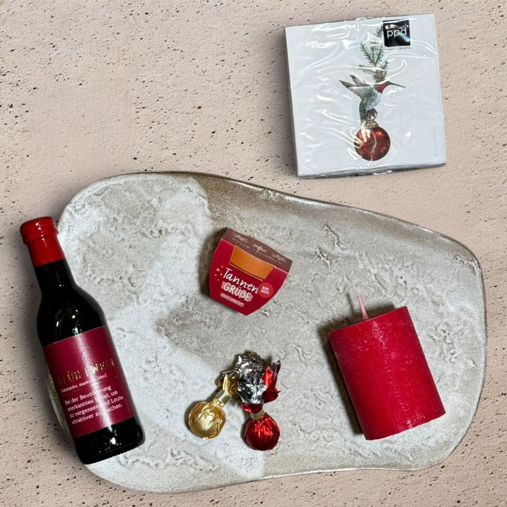 Ausgepacktes Glühwein Geschenkset mit Grafik Werkstatt Glühwein Flasche Venchi rote goldene Weihnachtskometen elegante rote Wachskerze Pflanztöpfchen Merry Christmas und ppd Franklin Cocktail Servietten