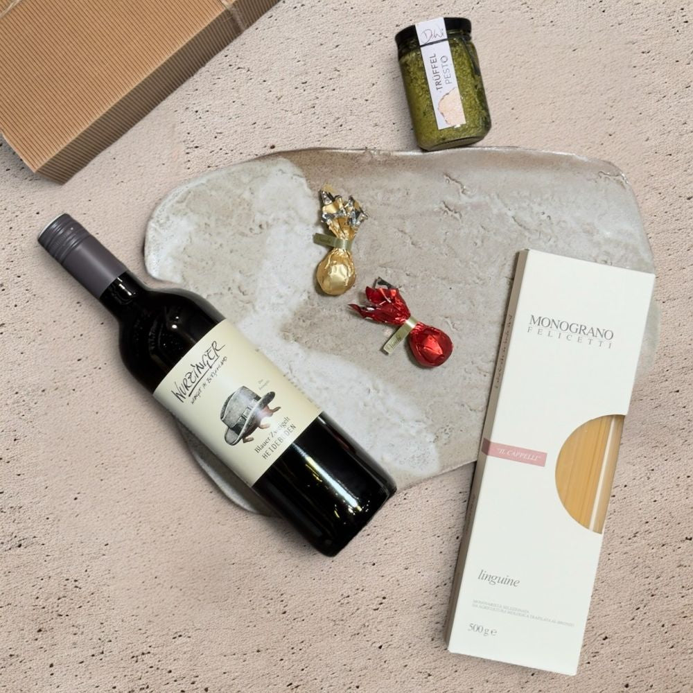 Ausgepackte Wein Geschenkbox Weihnachten mit Wurzinger Blauer Zweigelt Heideboden 2024 DeWi Pesto Trüffel Felicetti Monograno Il Cappelli Linguine 152 Venchi rote goldene Weihnachtskometen und Metall Weihnachtsmotive mit Schelle weiß gold